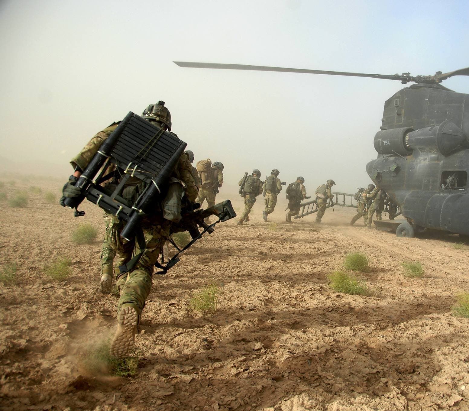 Special operations troops boarding a CH-47 Chinook helicopter in a dust cloud during a desert operation